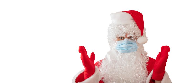 View of a man wearing a Santa Claus costume and medical mask with his arms, eyes wide open, isolated on white background. Man is upset. Banner size, copy space. New normal, pandemic holiday concepts.