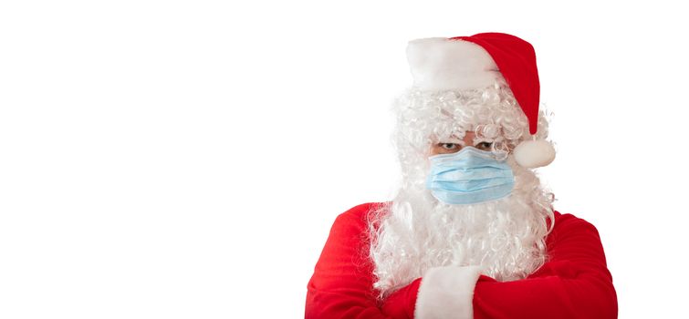 View of a man wearing a Santa Claus costume and medical mask with his arms crossed on his chest, isolated on white background. Banner size, copy space. New normal, pandemic holiday concepts.