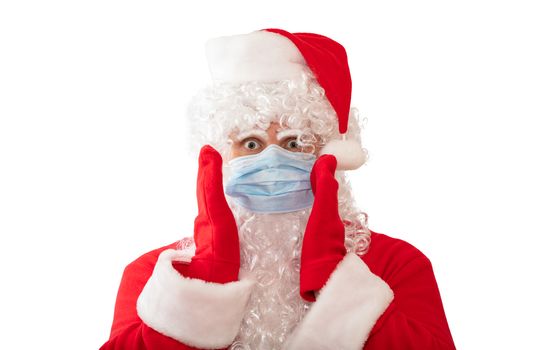 View of a man wearing a Santa Claus costume and medical mask with his arms by his face and eyes wide open, isolated on white background. Man looks scared. New normal, pandemic holiday concepts