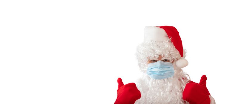 View of a man wearing a Santa Claus costume and medical mask with his thumbs up, isolated on white background. Man looks stressed. Banner size, copy space. New normal, pandemic holiday concepts