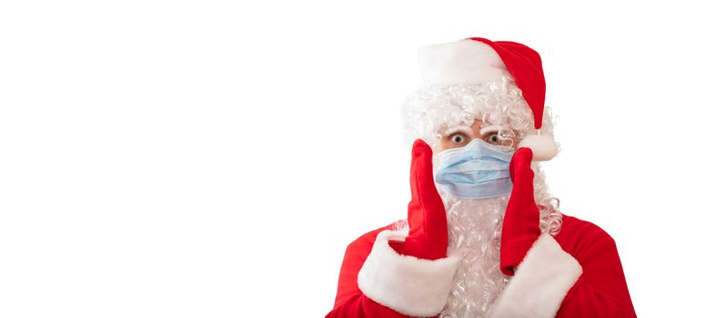 View of a man wearing a Santa Claus costume, medical mask with his arms by his face, eyes wide open, isolated on white background. Man looks scared. Banner size, copy space. Pandemic holiday concept.