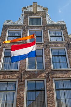 Old medieval townhouse with the national dutch flag and orange banner in Amsterdam the Netherlands