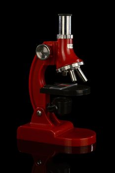 An isolated over a black reflective surface image of a red scientific microscope.