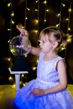 Cute little Child girl holding witch crystal ball with lightning and electricity over dark background with garlands bokeh