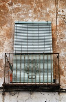 Old house facade with rusty balcony and green blind in Spain.