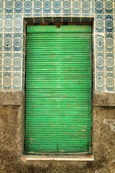 Old and damaged tiled facade in Lisbon. Closed Window with green blind