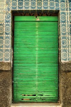 Old and damaged tiled facade in Lisbon. Closed Window with green blind