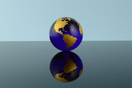 A crystal blue globe of the Earth over a reflective background.