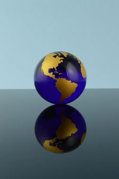 A crystal Blue globe of Earth over a reflective background.