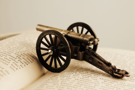 Closeup of an open book with a war cannon ontop using a vintage effect.