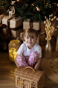 .Girl in pajamas sits on the floor in front of the Christmas tree and plays.