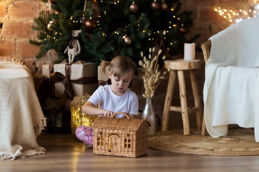 .Girl in pajamas sits on the floor in front of the Christmas tree and plays.
