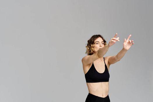 A slender woman in black leggings on a gray background gestures with her hands gymnastics sports. High quality photo