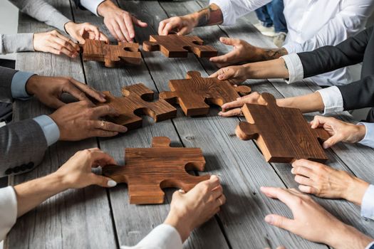 Business people team sitting around meeting table and assembling wooden jigsaw puzzle pieces unity cooperation ideas concept