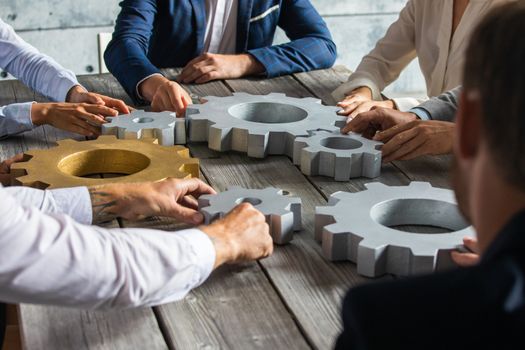 Group of business people joining together silver and golden colored gears on table at workplace