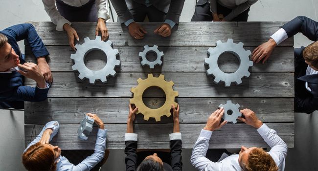 Group of business people joining together silver and golden colored gears on table at workplace top view