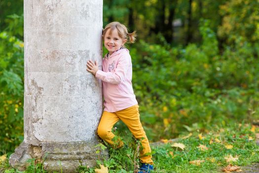 .A girl with a broken arm stands near a column in an old park on an autumn walk