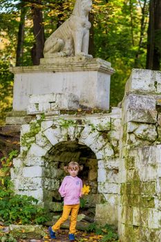 A girl with a broken arm stands near a brick wall in an old park on an autumn walk