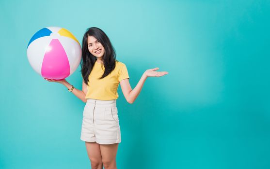 Happy Asian young beautiful woman smiling white teeth standing wear shirt her holding beach ball in summer holiday travel isolated studio shot on blue background with copy space for text