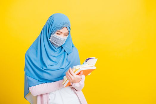 Asian Muslim Arab, Portrait of happy beautiful young woman religious wear veil hijab and face mask protective to prevent coronavirus she hold book on hand and open reding it on yellow, Back to college