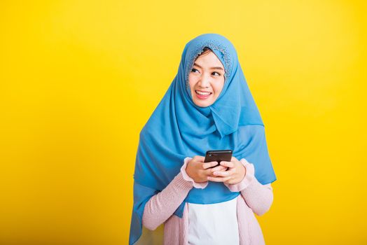 Asian Muslim Arab, Portrait of happy beautiful young woman Islam religious wear veil hijab funny smile she using hold mobile smart phone reading social media isolated on yellow background