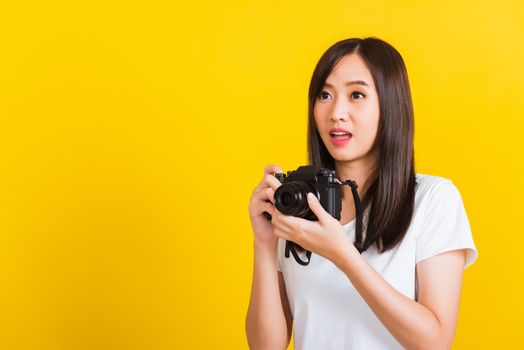 Portrait of happy Asian beautiful young woman photographer holding vintage digital mirrorless photo camera on hands, studio shot isolated on yellow background, lifestyle teenager hobby travel concept