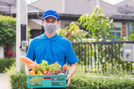 Asian grocery store delivery man wearing blue uniform and face mask protect he delivering fresh food vegetable in plastic box at door front home after coronavirus outbreak, back to new normal concept