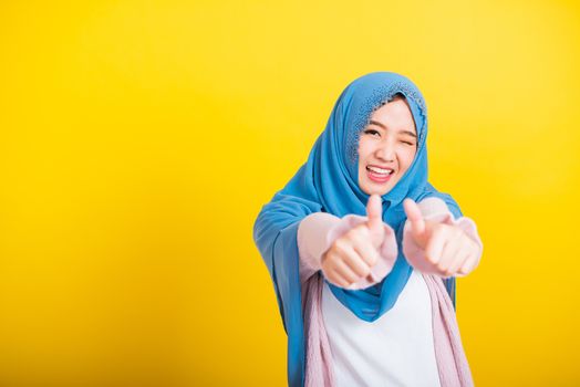 Asian Muslim Arab, Portrait of happy beautiful young woman Islam religious wear veil hijab funny smile she made finger thumbs up, Ok sign to agree, studio shot isolated on yellow background