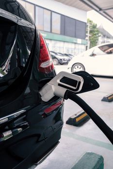 power supply connects to plug-in electric vehicle or electric car at charging station in car park area of shopping plaza. charging technology for future automotive and city life.
