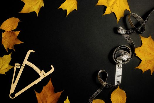 Autumn fallen leaves, measuring tape and caliper on black background