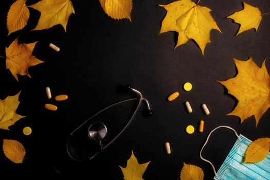 Autumn fallen leaves and medical masks and medicines on black background