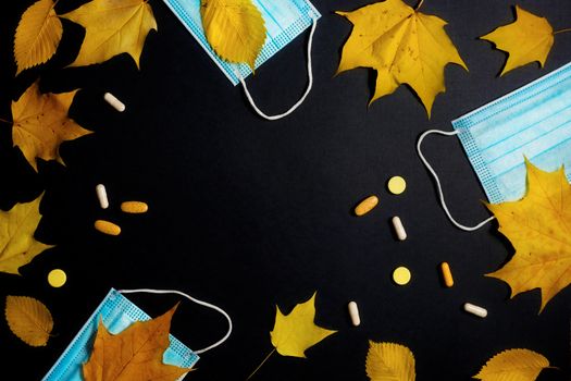 Autumn fallen leaves and medical masks and medicines on black background