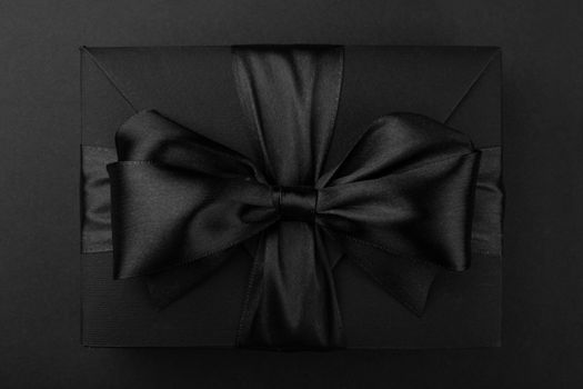Black friday gift, paper box with silk ribbon bow on black paper background with copy space for text, flat lay top view template