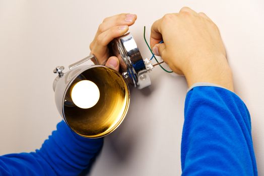 Male electrician connects the wall lamp at domestic house