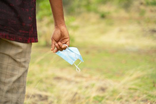 Closeup of hands holding medical mask with copy space - concept of removing mask to feel nature during coronavirus or covid-19 pandemic on top of mountain