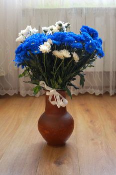 a bouquet of blue and white chrysanthemums in a clay vase on the wooden floor