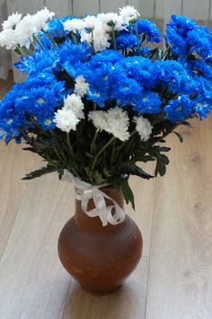 a bouquet of blue and white chrysanthemums in a clay vase on the wooden floor