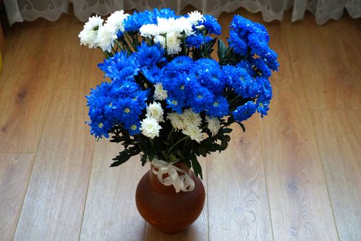 a bouquet of blue and white chrysanthemums in a clay vase on the wooden floor