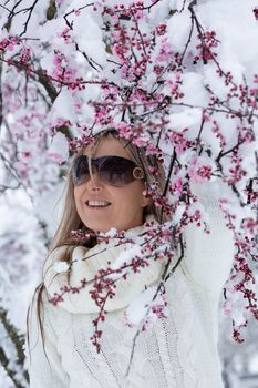 Woman stands under cherry blossom tree blooming with fresh winter snow