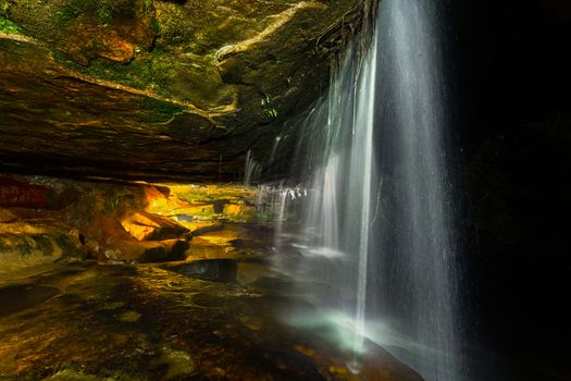 Waterfall flowing over a cave in the night,  the inside lit by warm light 