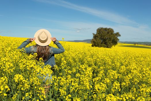 Female in denim jacket and shorts  in a field of flowering canola growing in rural outskirts of Australia