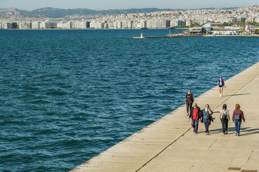 Unidentified persons with face protection walk on the pedestrian area of the city waterfront.