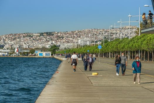Unidentified persons with face protection walk on the pedestrian area of the city waterfront.