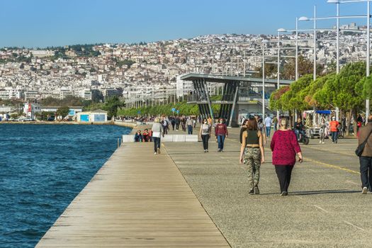 Unidentified persons with face protection walk on the pedestrian area of the city waterfront.