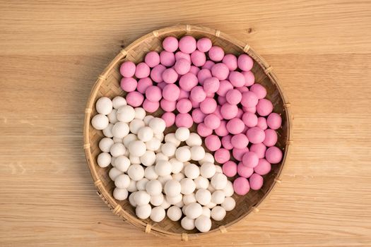 Raw little red and white tangyuan in a sieve over wooden table, concept of preparing food for winter solstice festival.
