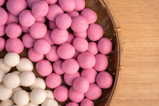 Raw little red and white tangyuan in a sieve over wooden table, concept of preparing food for winter solstice festival.