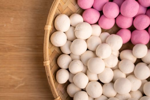 Raw little red and white tangyuan in a sieve over wooden table, concept of preparing food for winter solstice festival.