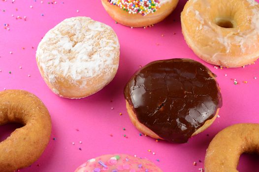 A closeup of various donuts over a hot pink background.