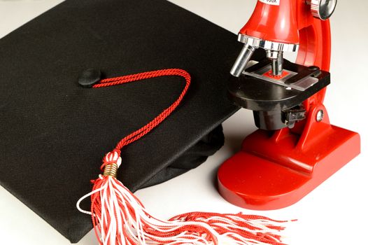 A grad hat and microscope over a white background.