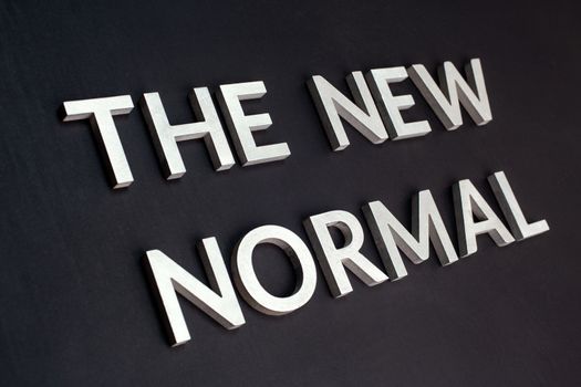 words the new normal laid with silver metal letters on flat black matte surface in tilted perspective with dark lightiing